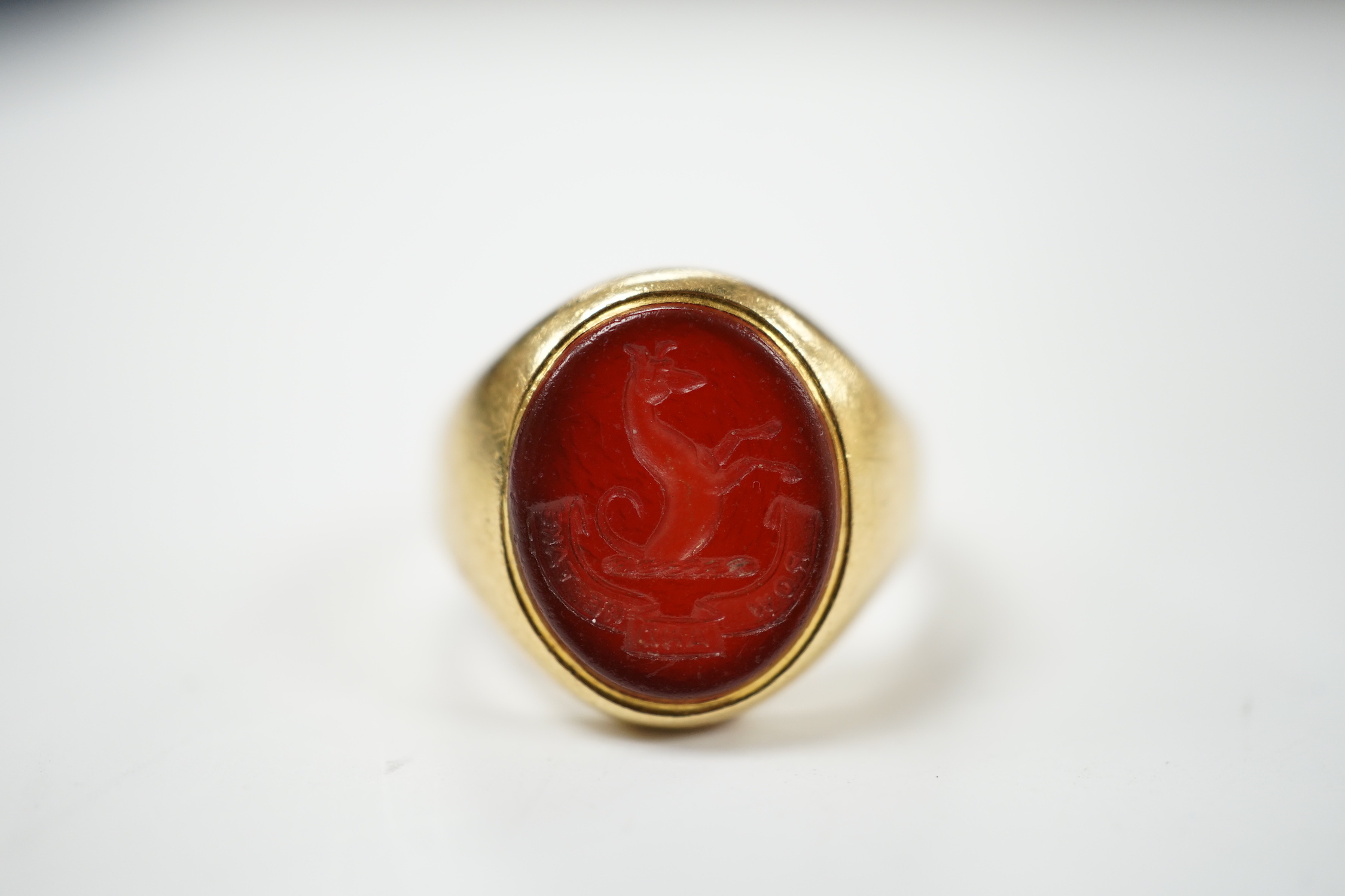 An 18ct and oval intaglio carnelian set signet ring, carved with family crest and motto, size K, gross weight 6.9 grams.